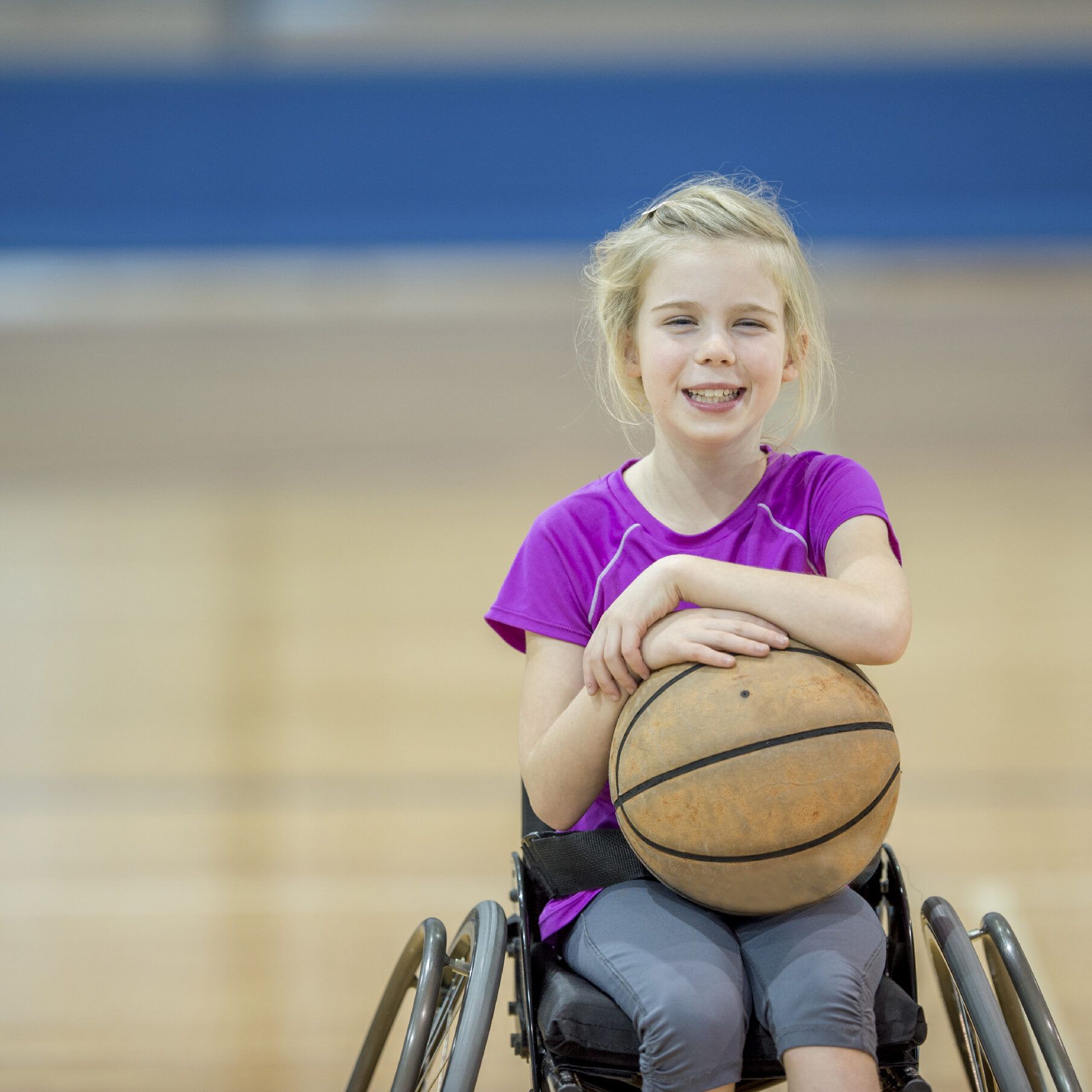 A little girl with a physical disability is playing basketball in her wheelchair.